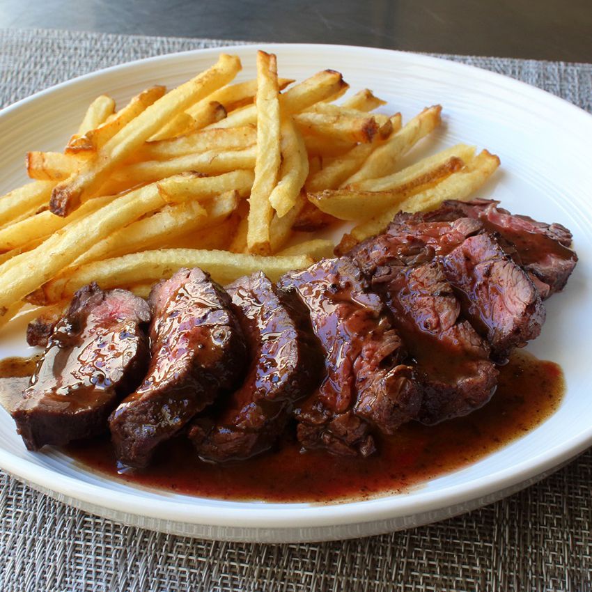 Close up view of a sliced Butcher's Steak (Hanger Steak) with sauce, served with french fries on a white plate