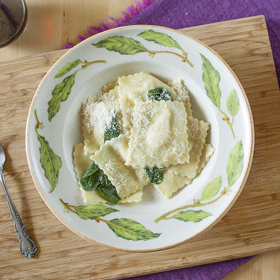 Close up view of Pear and Gorgonzola Ravioli with thyme in a green and white bowl on a wooden cutting board