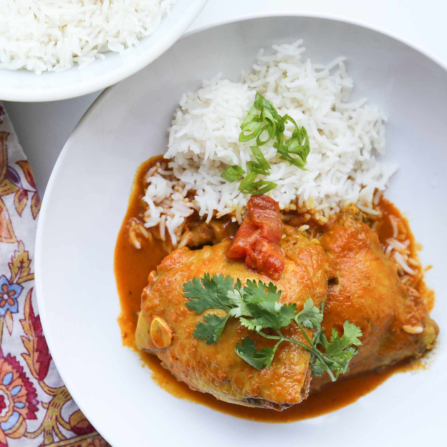 Top-down view of chicken curry in a white bowl with Basmati rice, garnished with cilantro