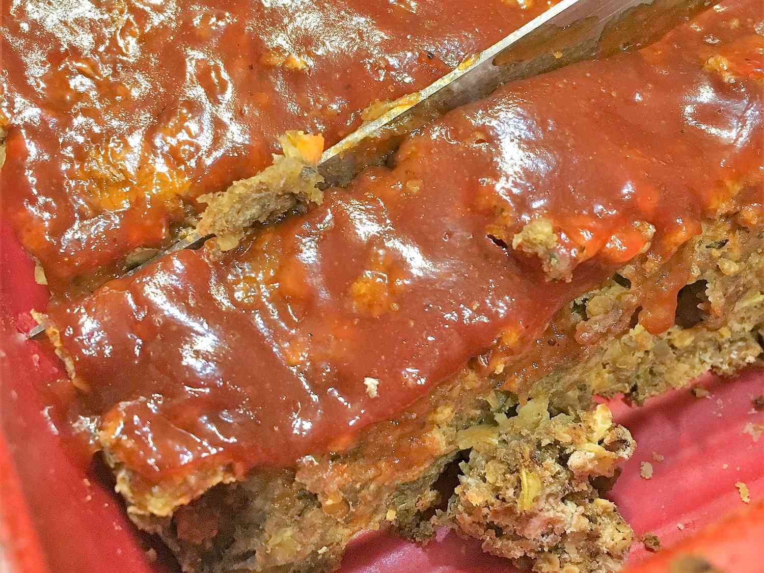 Close up view of a sliced Lentil Loaf with a knife in a red baking dish