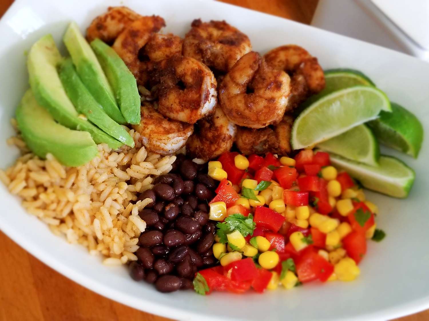 Close up view of a Grain Bowl with Blackened Shrimp, Avocado, and Black Beans, served with limes on a white platter