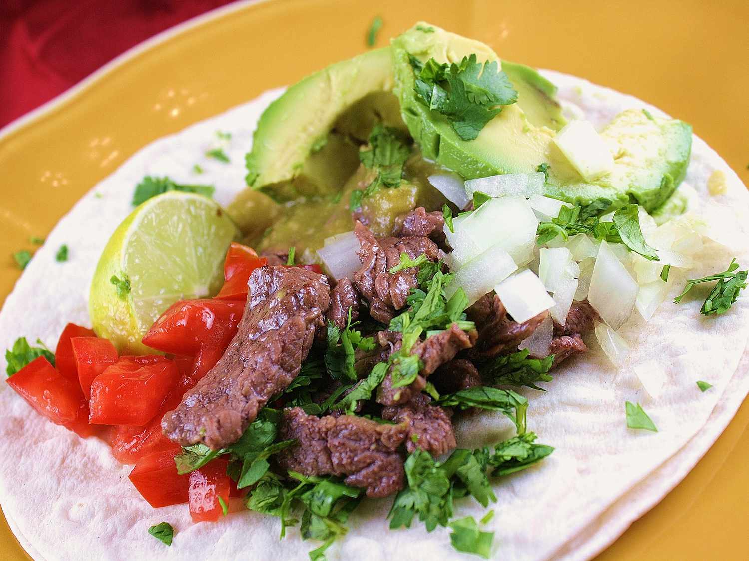 Close up view of a Carne Asada Taco garnished with fresh herbs on a yellow plate