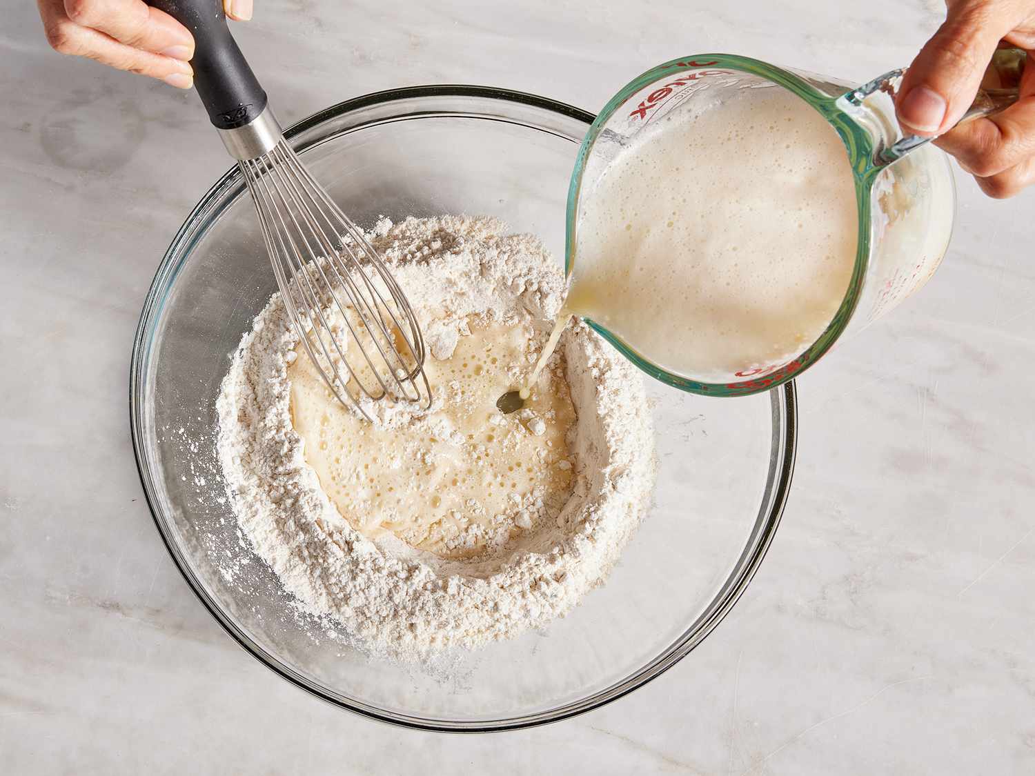 Overhead of a beer mixture being poured and whisked into a flour mixture in a bowl. 