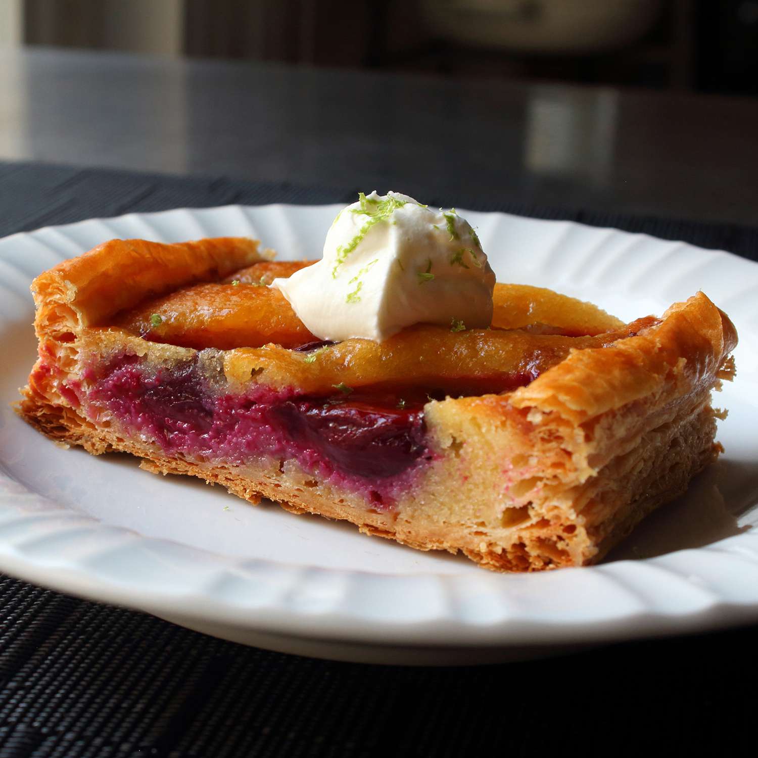 Close up view of a slice of Fresh Fruit Frangipane Tart garnished with cream and lime zest on a white plate