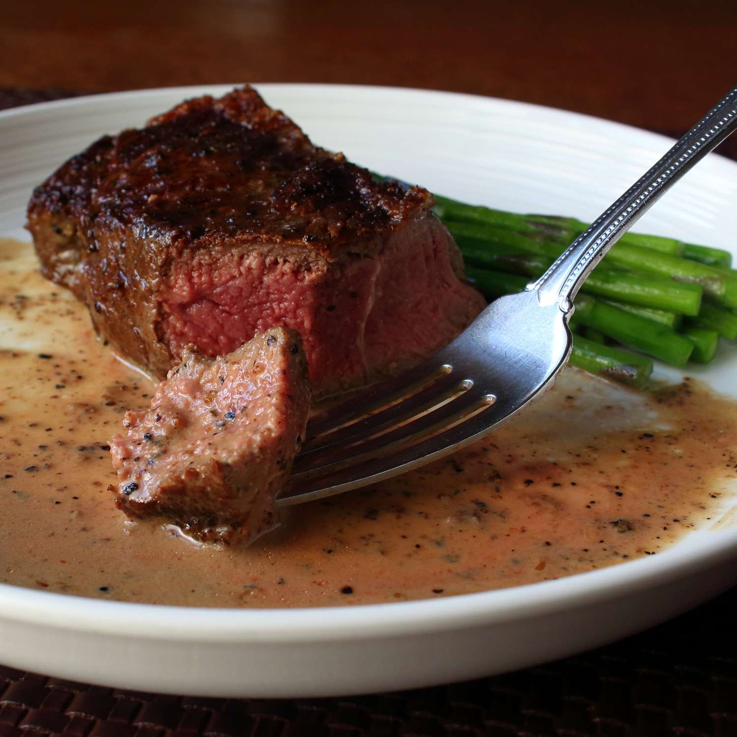 Close up view of a Bourbon Pepper Pan Sauce on a plate with a steak, asparagus, and a fork