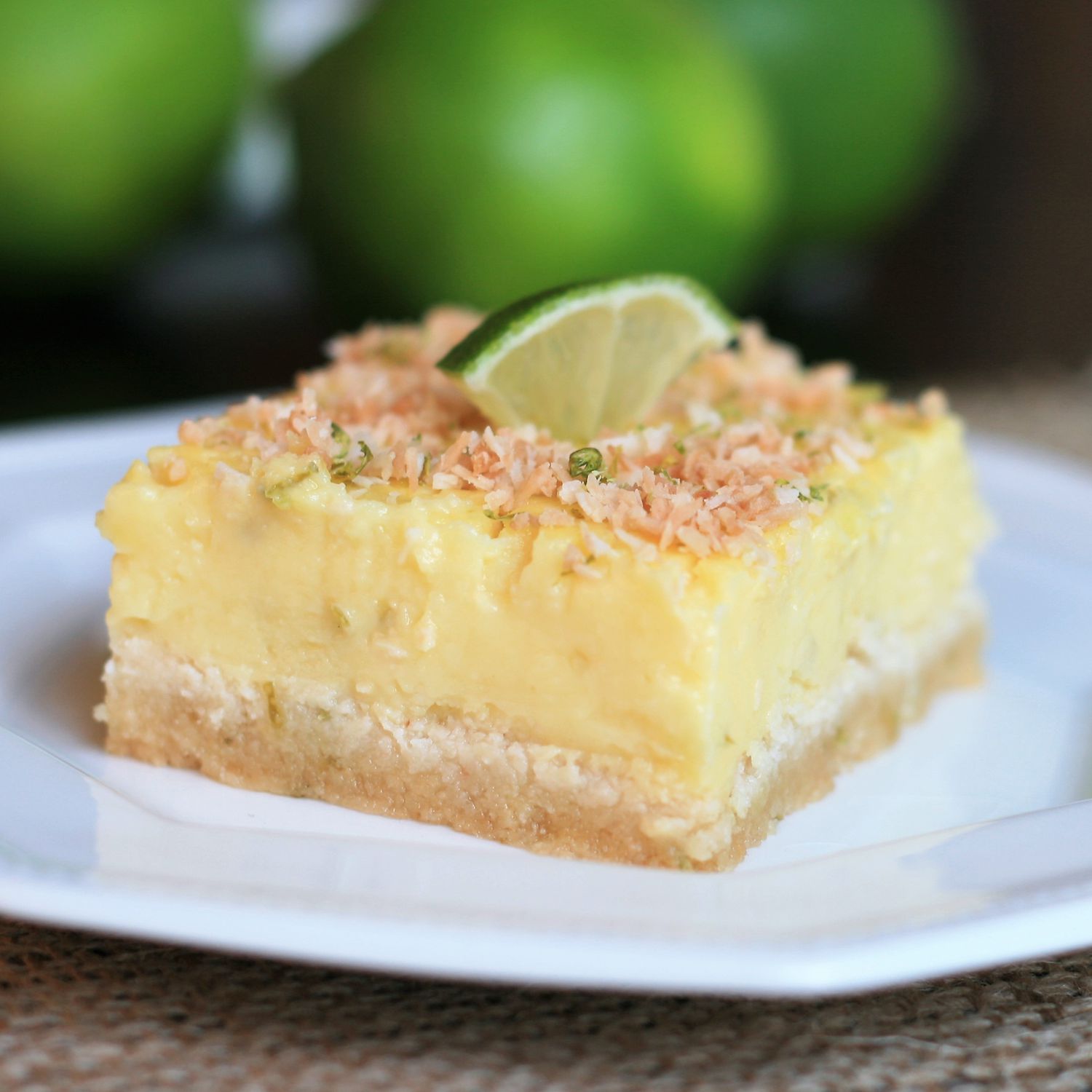 Close up view of a Low-Carb Coconut Lime Bar, garnished with toasted coconut, lime zest, and a slice of lime, on a white plate