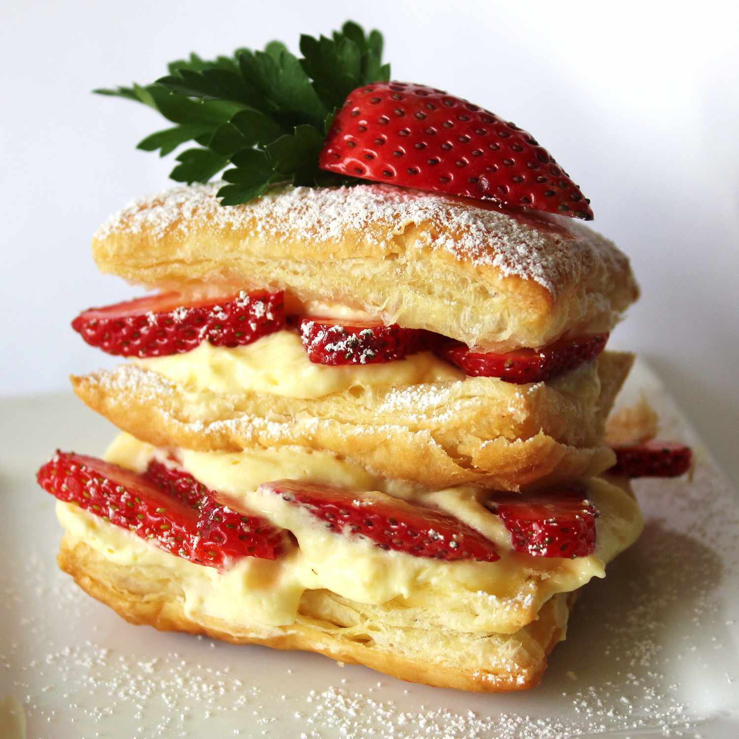 Close up view of Strawberry Napoleons with sliced strawberries and cream, garnished with powdered sugar on a white plate