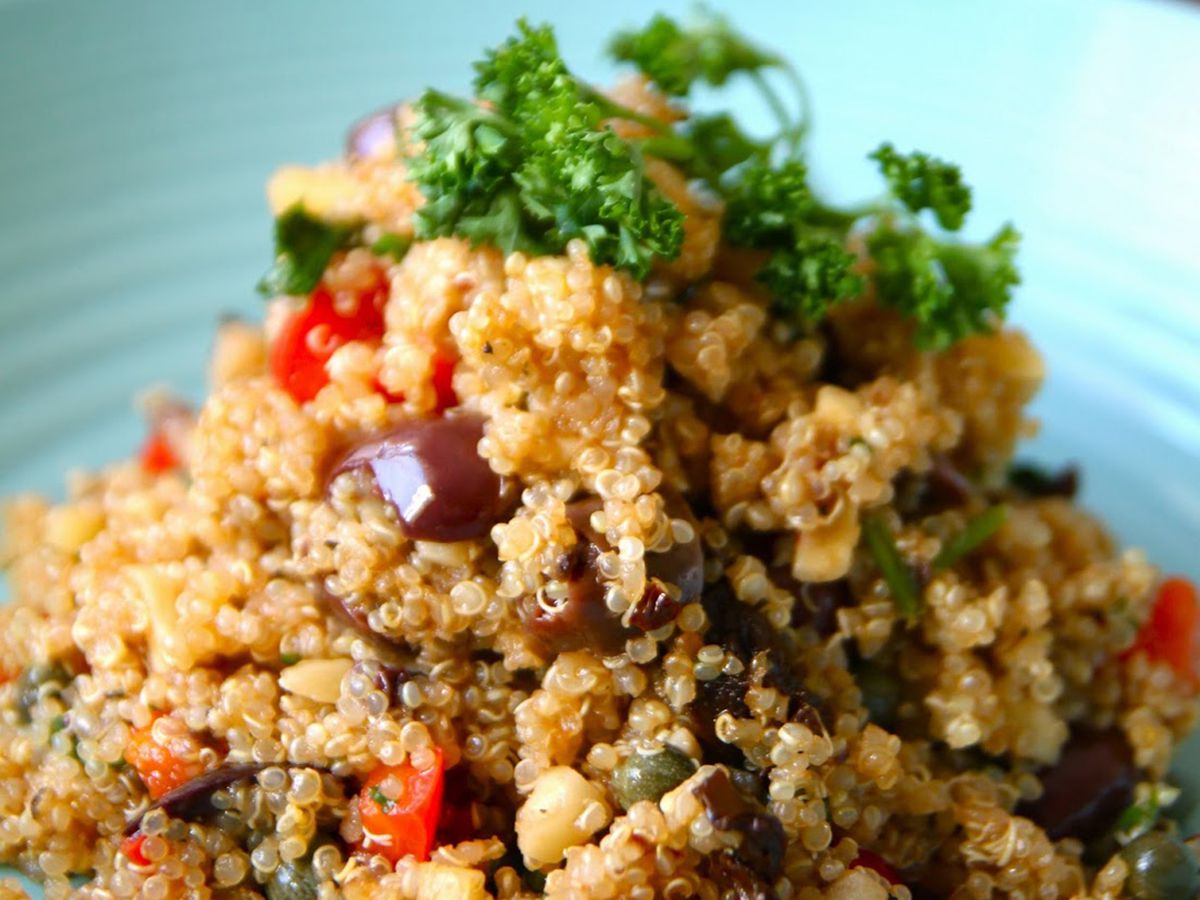 Close up view of Warm Quinoa Salad with olives, peppers and capers, garnished with fresh herbs, on a blue plate