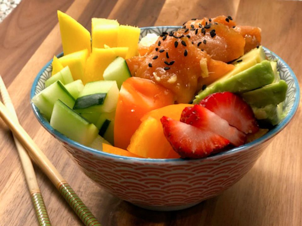 Close up view of a Smoked Salmon Poke Bowl with avocado, cucumbers, strawberries, and other fruit in a bowl