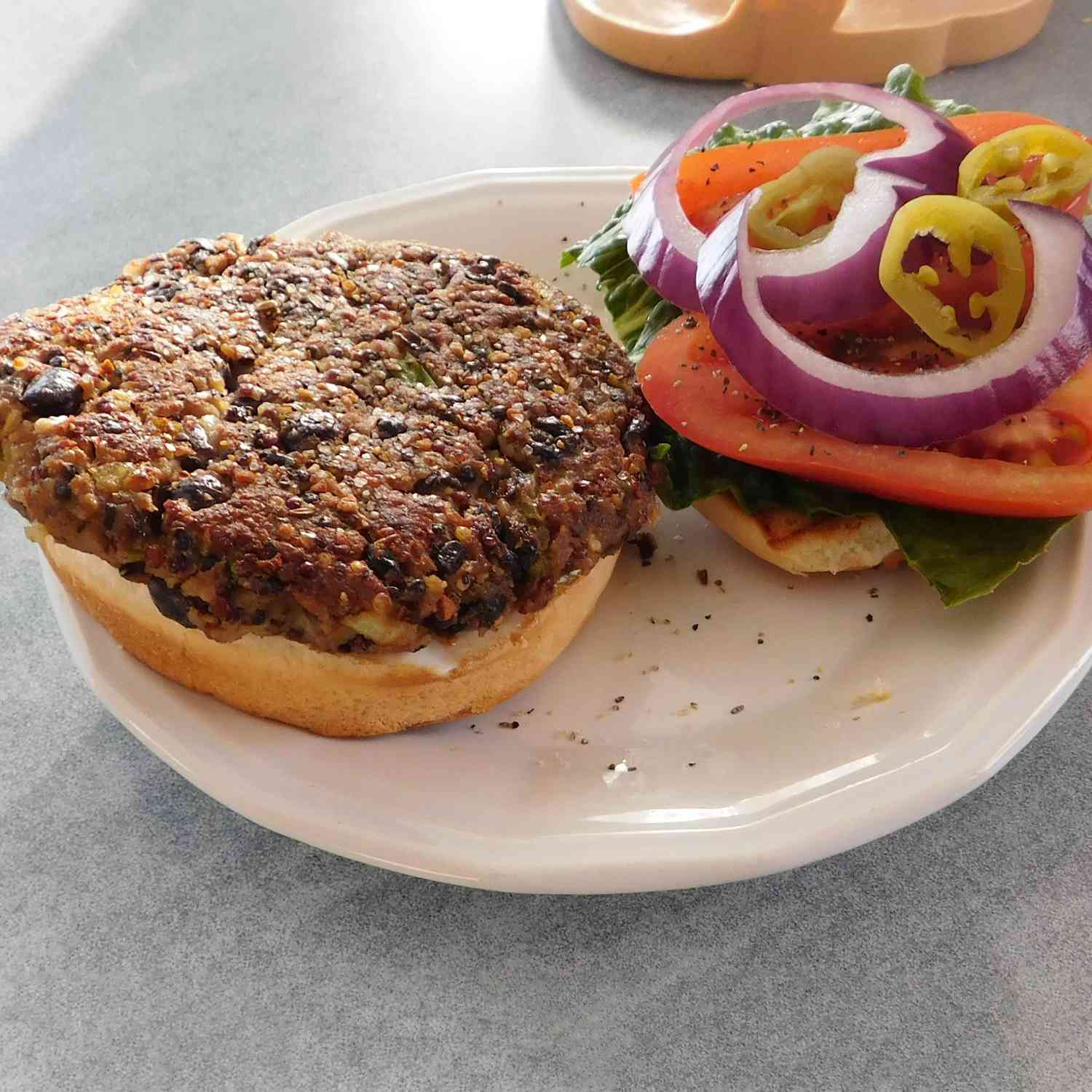 Close up view of a Quinoa Black Bean Burgers on a bun with toppings, on a white plate