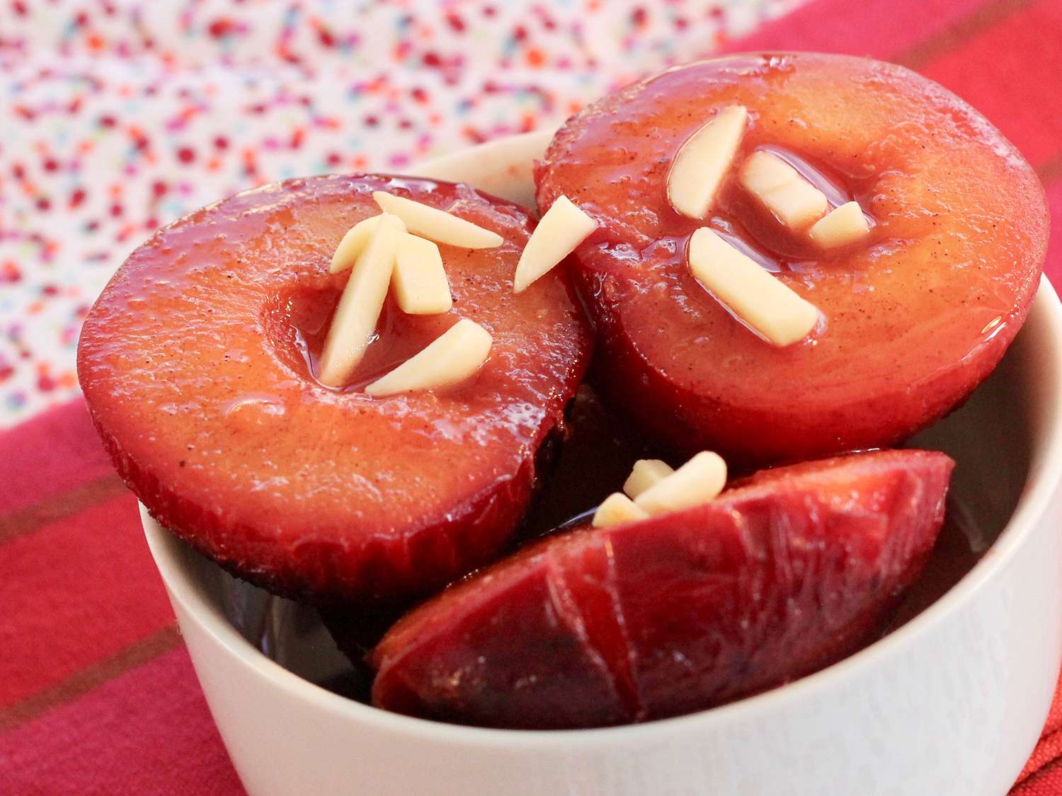 Close up view of Spicy Oven-Roasted Plums garnished with nuts in a white bowl
