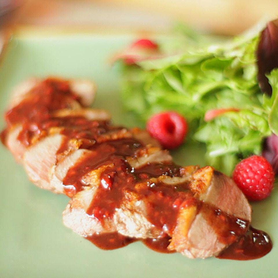 Close up view of sliced Duck Breast garnished with Raspberry Sauce, served with a salad with fresh raspberries on a green plate