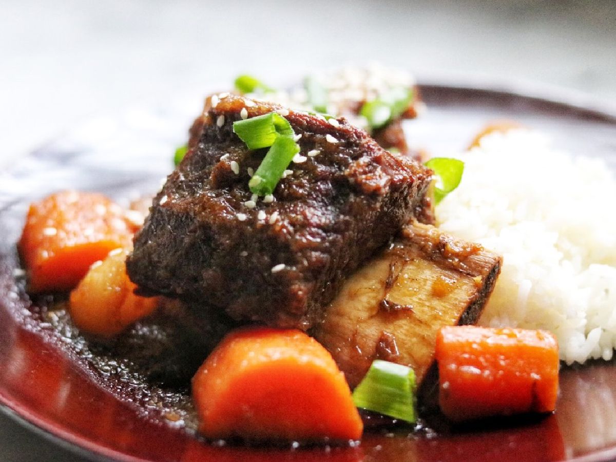 Close up view of Galbi (Korean-Style Short Ribs) with carrots and white rice, garnished with green onions on a plate