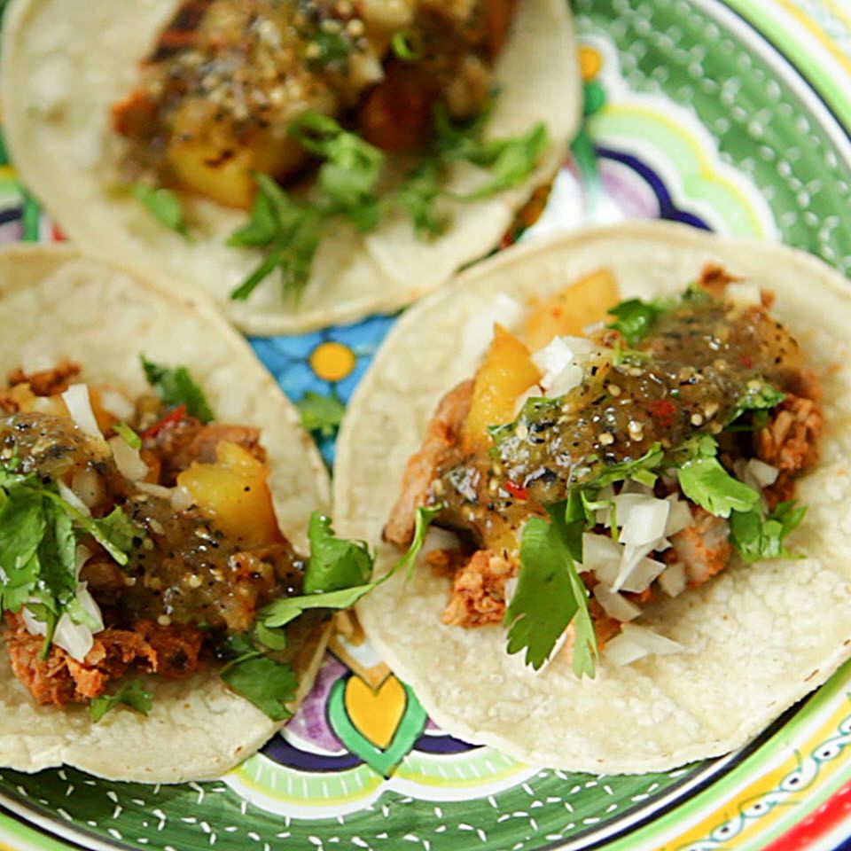 Close up view of Tacos al Pastor garnished with fresh herbs on a colorful plate