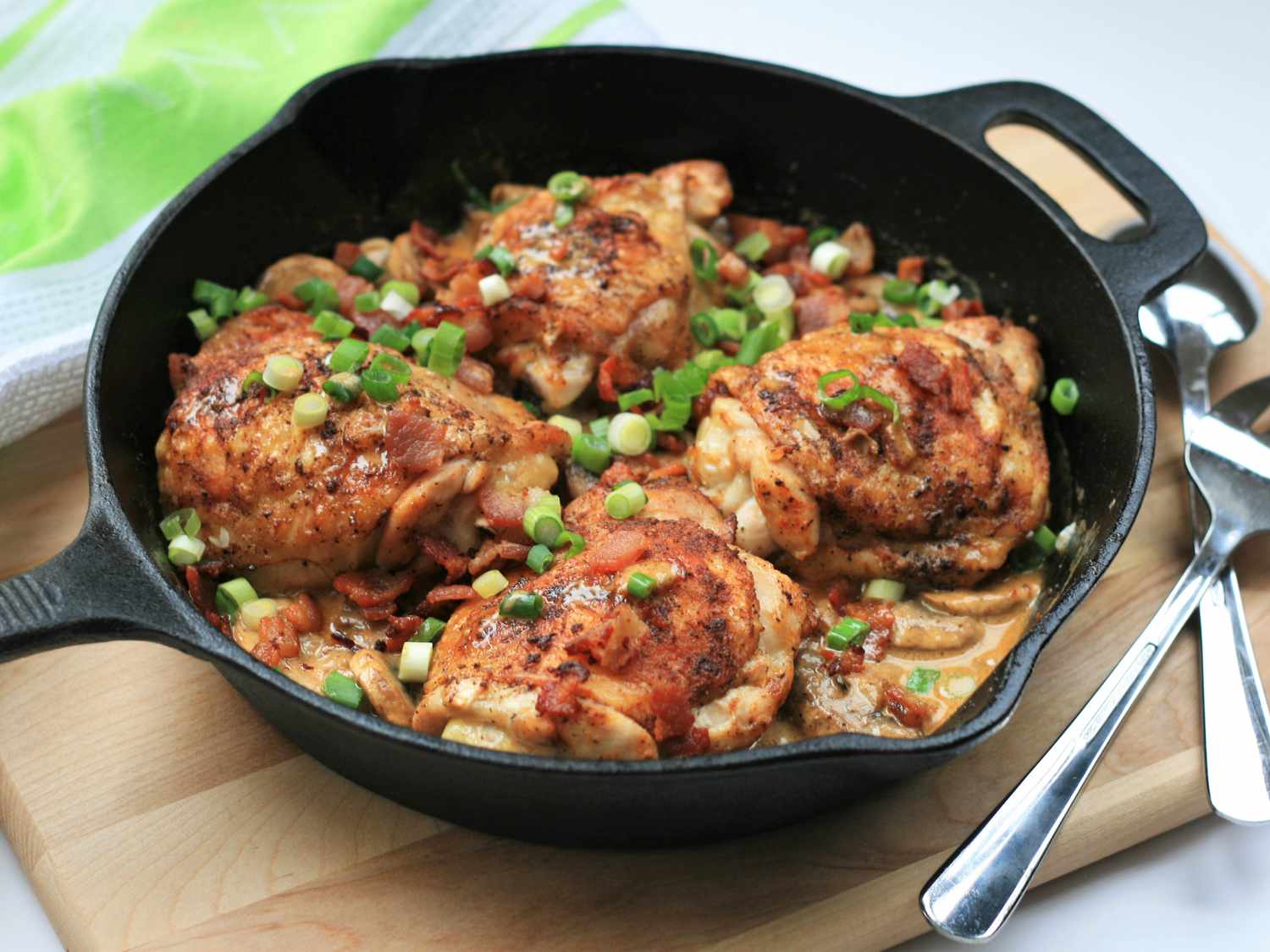 Close up view of Keto Smothered Chicken Thighs garnished with green onions in a cast iron pan