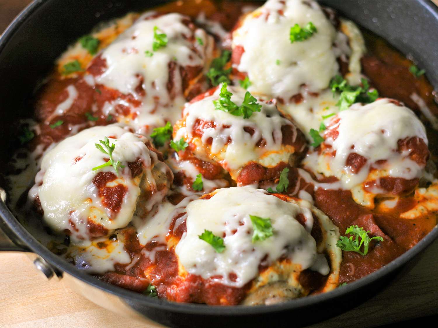 Close up view of Baked Italian Chicken Thighs garnished with fresh herbs in a cast iron skillet