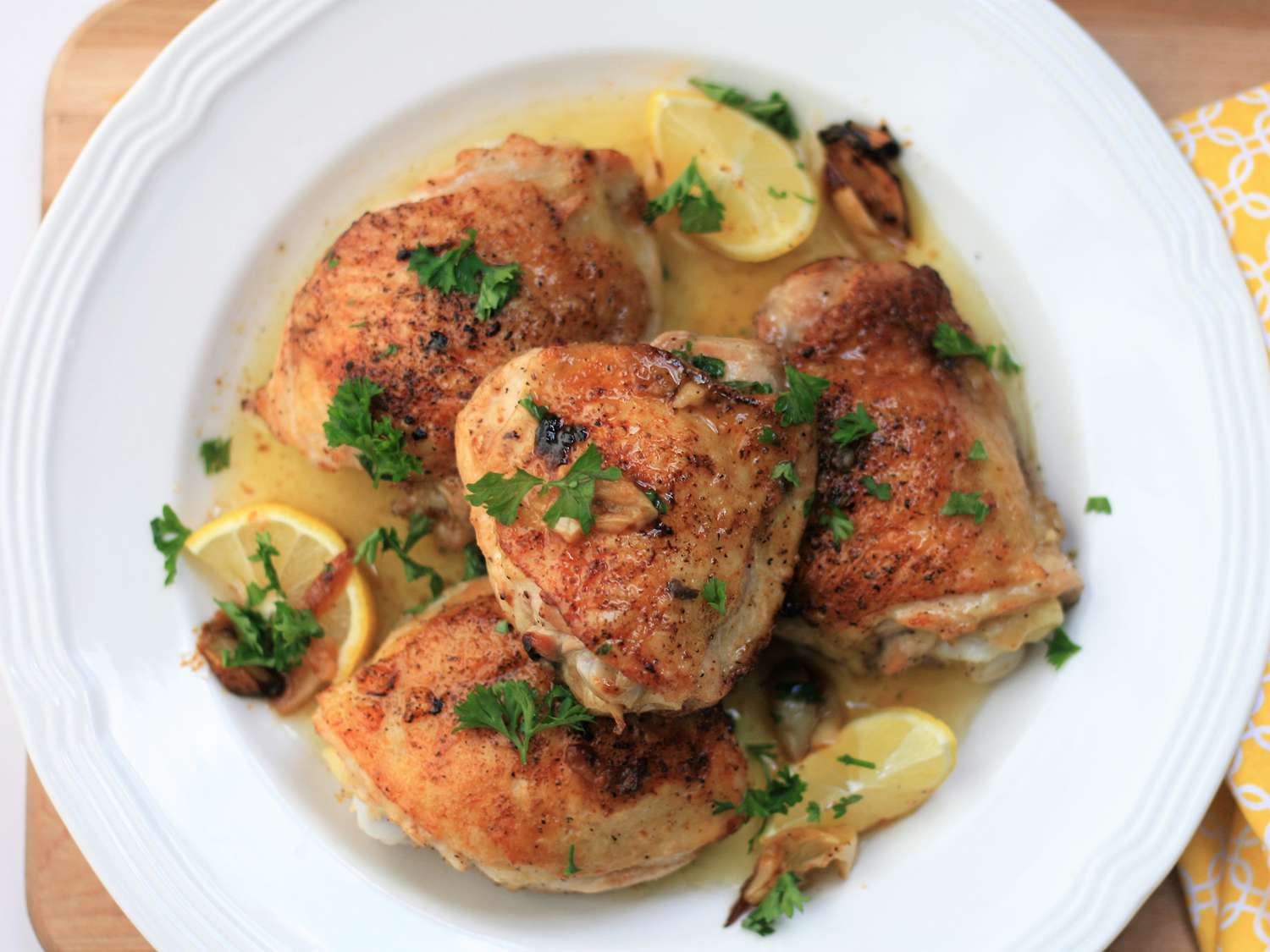 Overhead view of Baked Lemon-Butter Chicken Thighs garnished with fresh herbs and lemon wedges in a white bowl