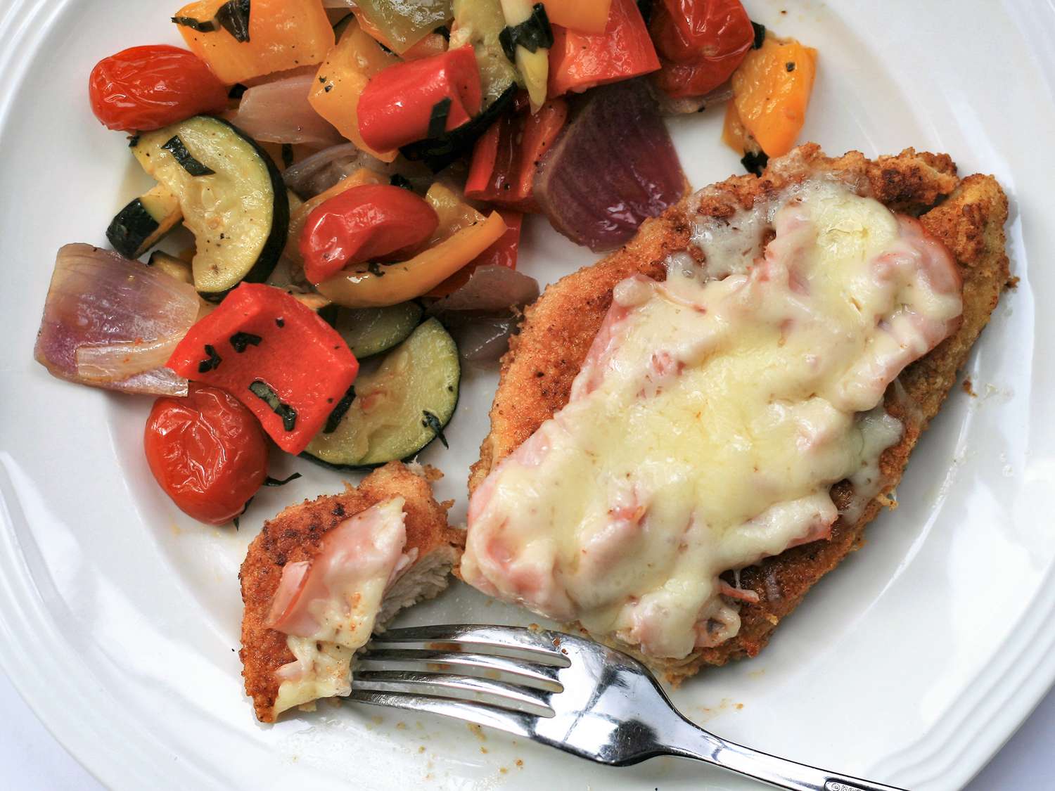 Close up view of a Keto Open-Faced Chicken Cordon Bleu, served with zucchini, peppers, onions, tomatoes and herbs on a plate with a fork