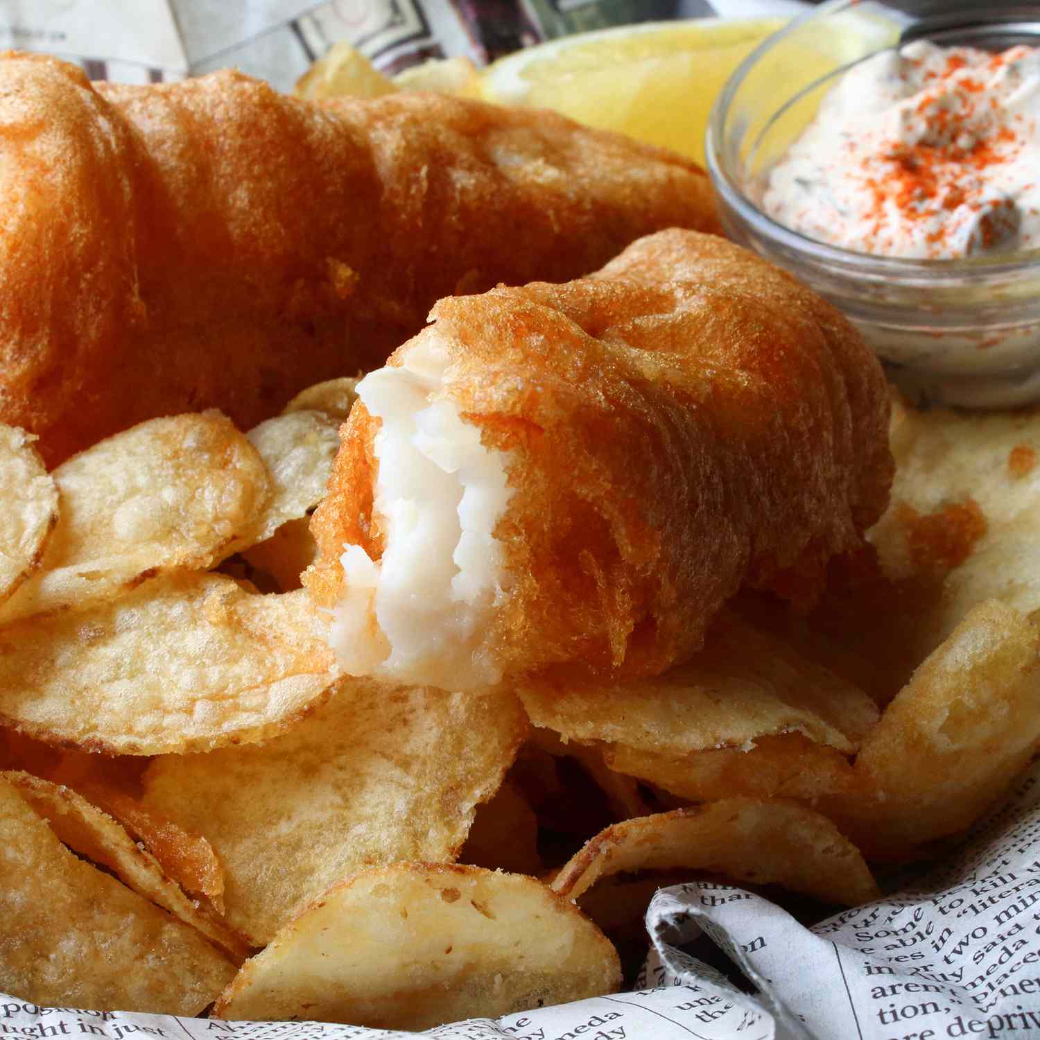 Close up view of Crispy Beer Batter Fish & Chips with sauce in a bowl