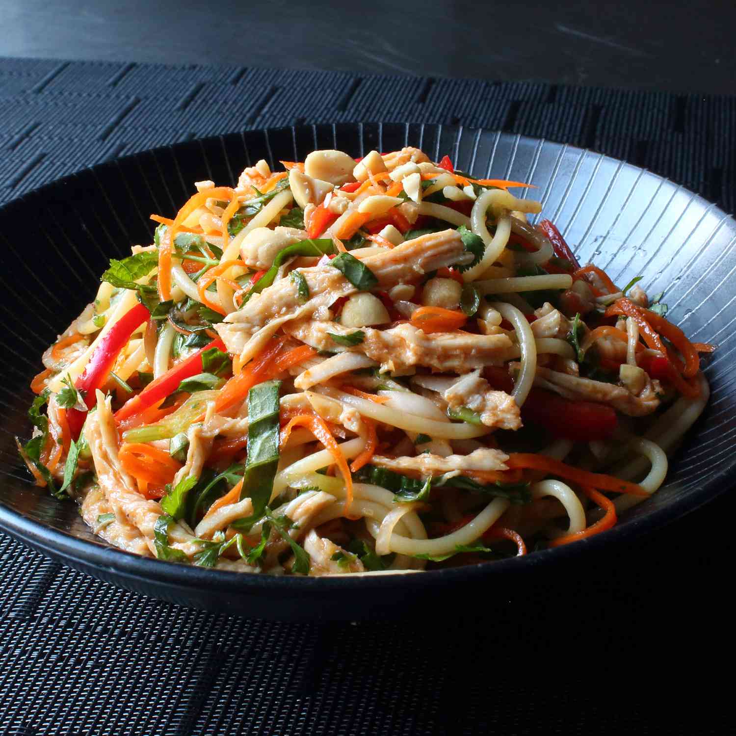 Close up view of Chicken Noodle Salad with peppers, carrots and lettuce in a black bowl