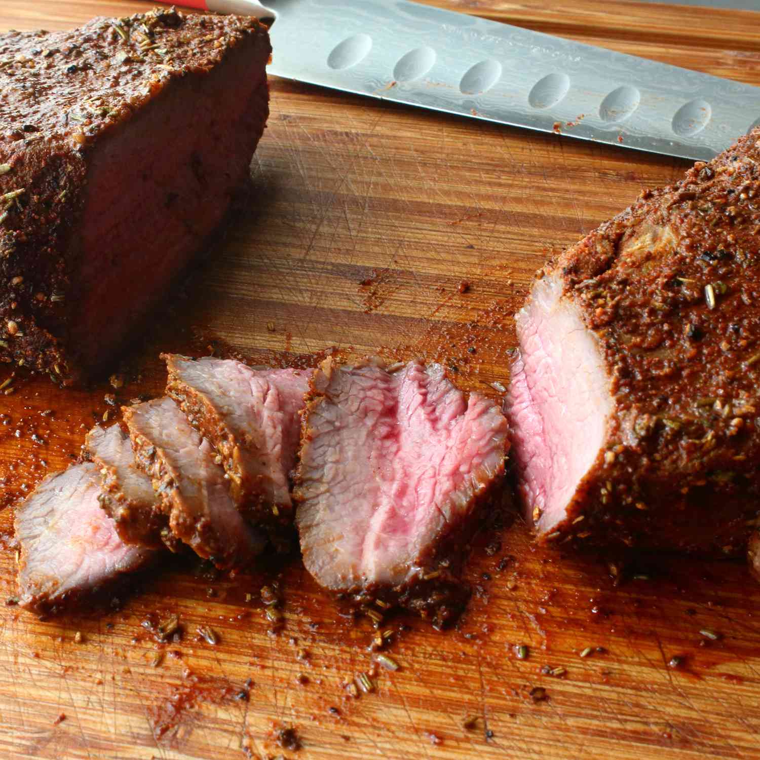 Close up view of beef tri-tip sliced on a wooden cutting board with a knife