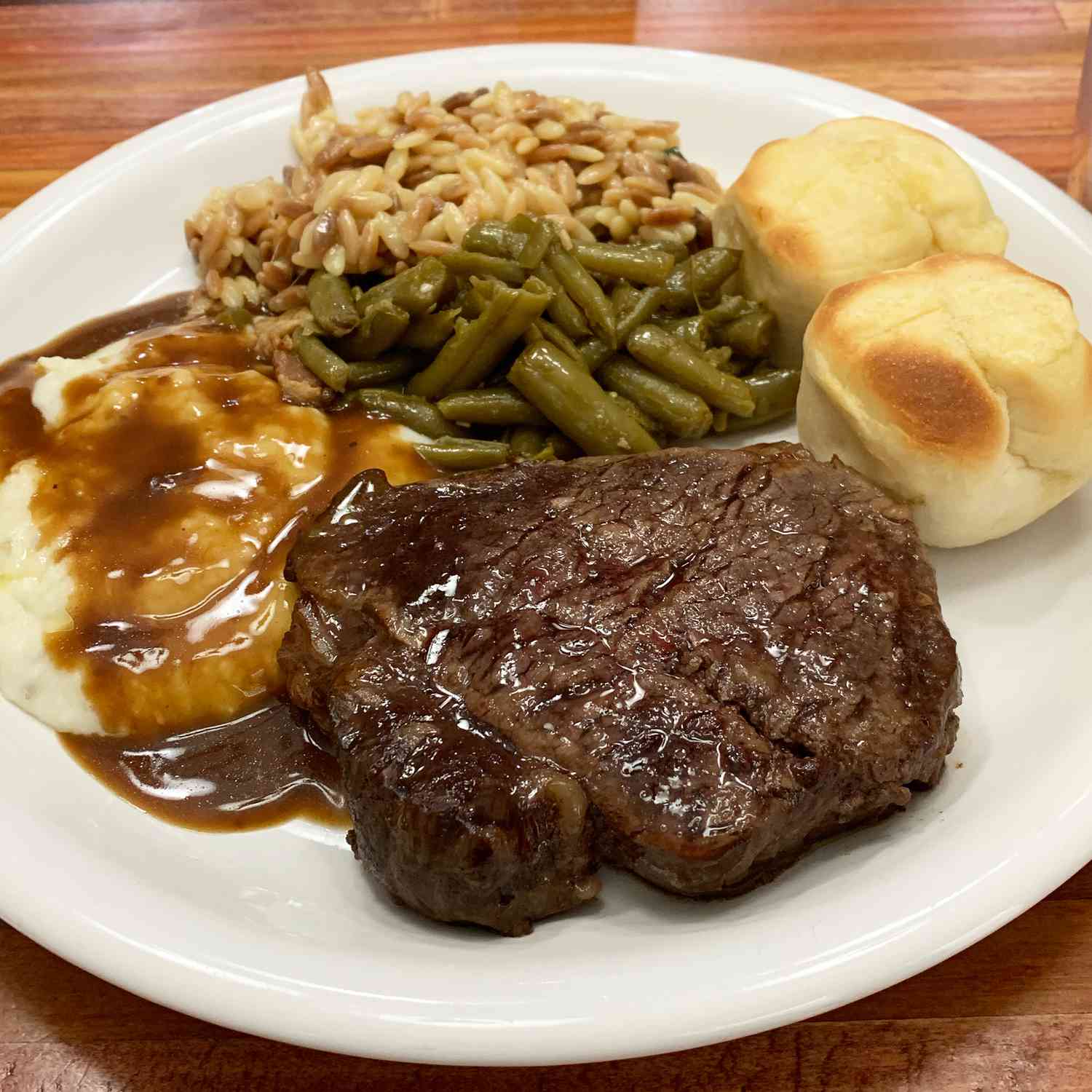 Close up view of a Fabulous Beef Tenderloin steak on a plate with mashed potatoes with gravy, green beans, rice, and buns