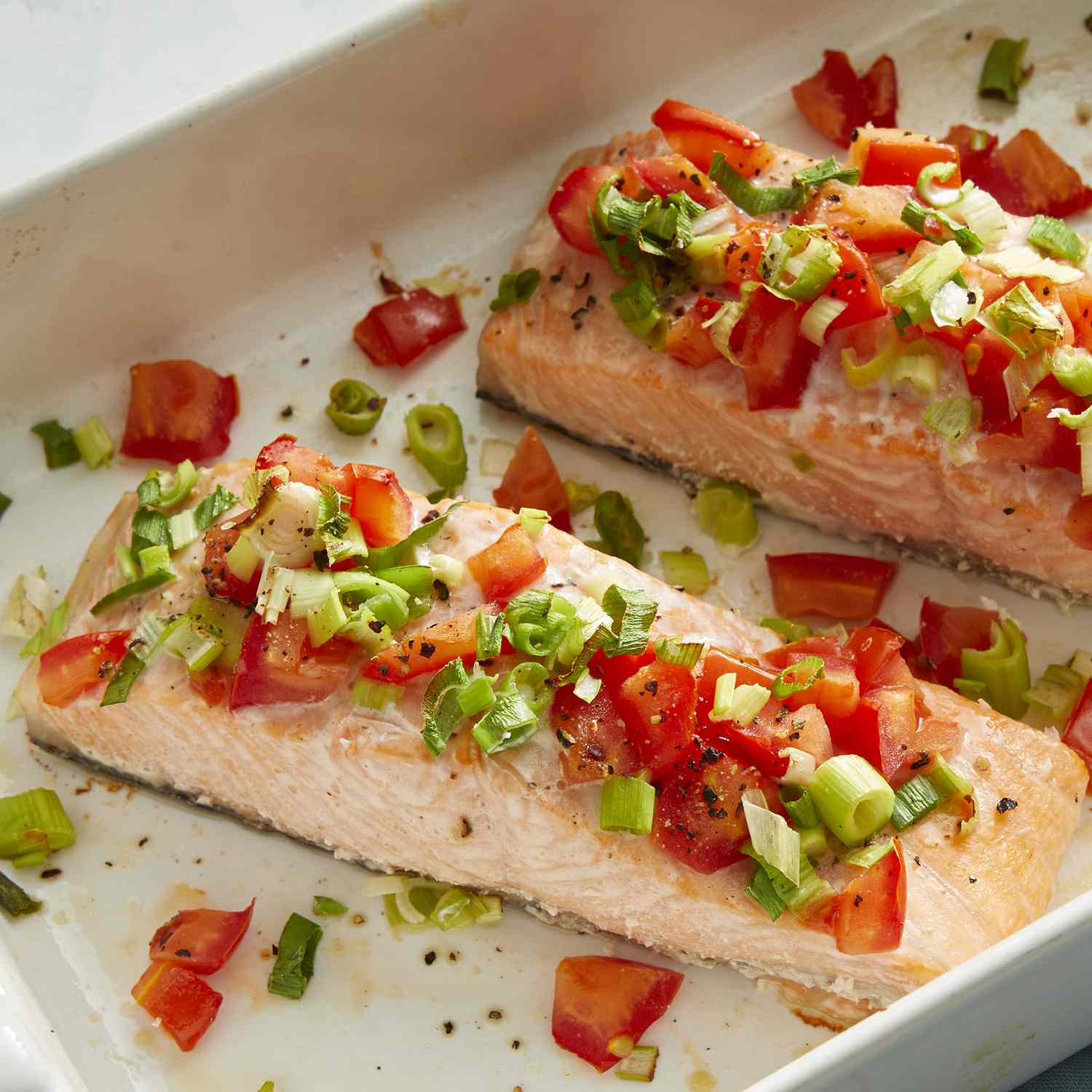 Mid angle looking at a few salmon fillets in a casserole dish, topped with chopped tomatoes and green onions