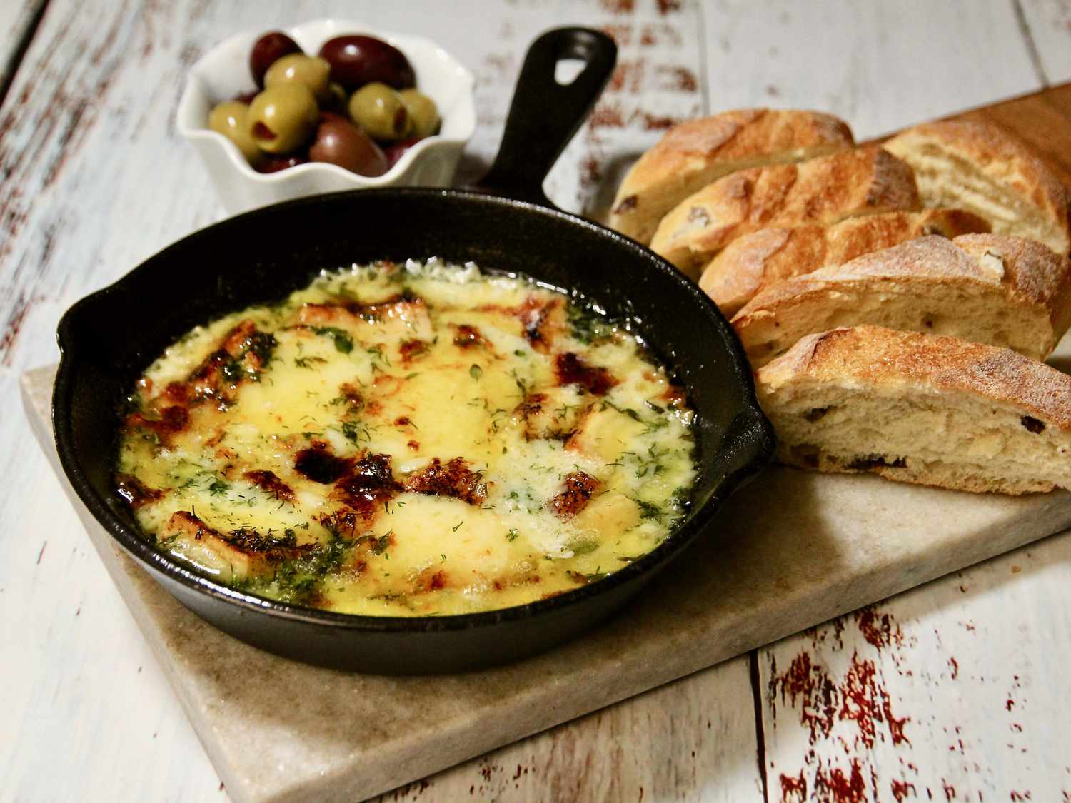 Baked gruyere cheese in cast iron pan with bread and olives