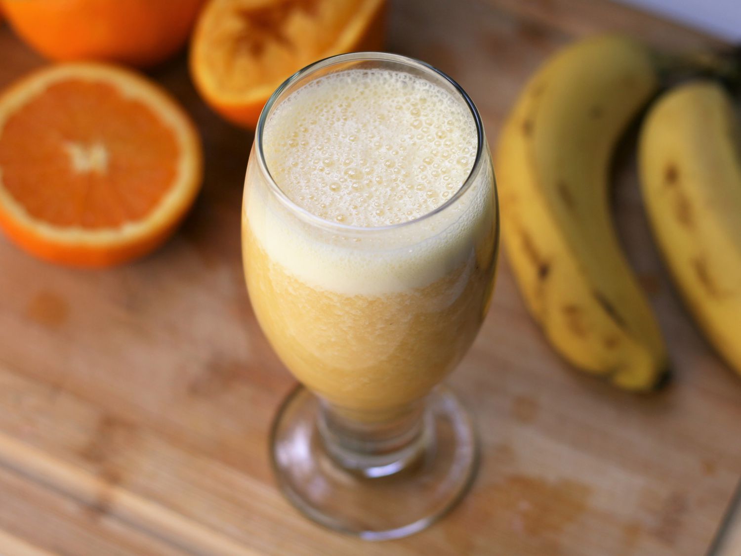 Juice with foam top and oranges and bananas in background