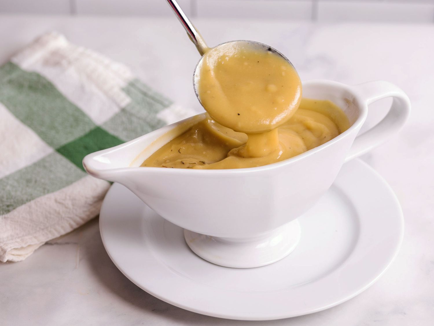 A low angle view of a spoonful of gravy being lifted out of a white gravy boat.