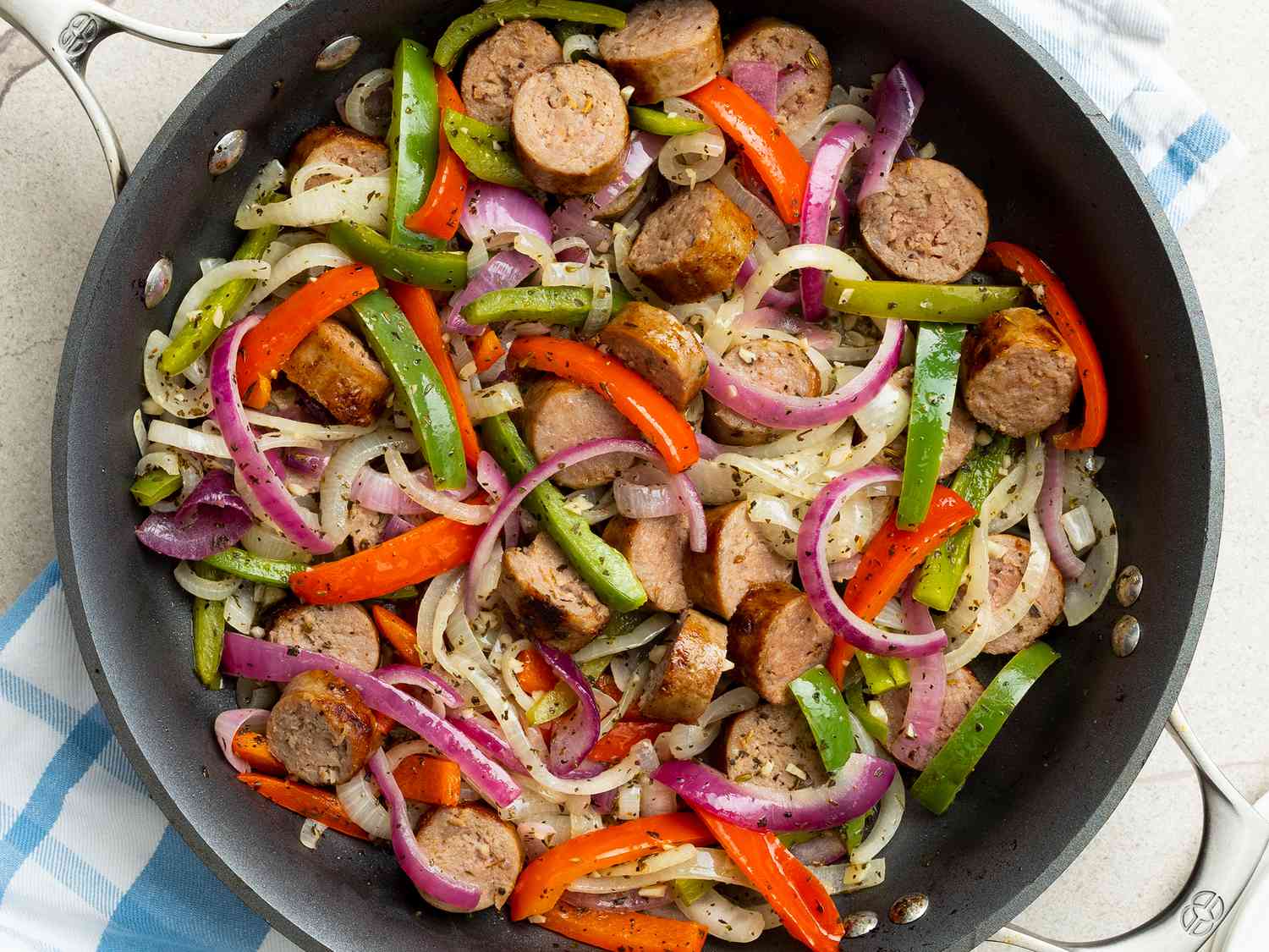 Overhead view looking into a skillet of Italian sausage, peppers and onions.