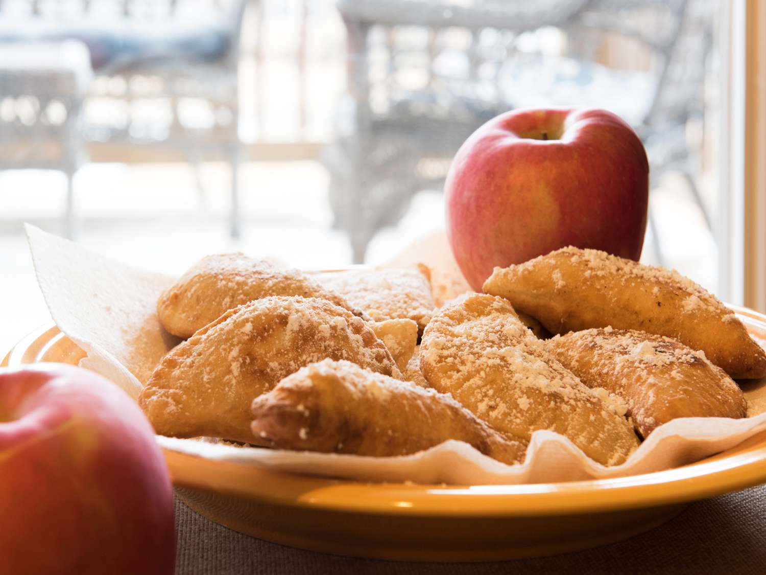 Close up view of Fried Apple Pies on a paper towel lined plate with an apple in the background