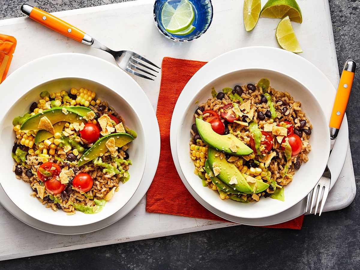 Close up view of Rice and Bean Bowls garnished with avocado and tomatoes in white bowls next to lime wedges and forks