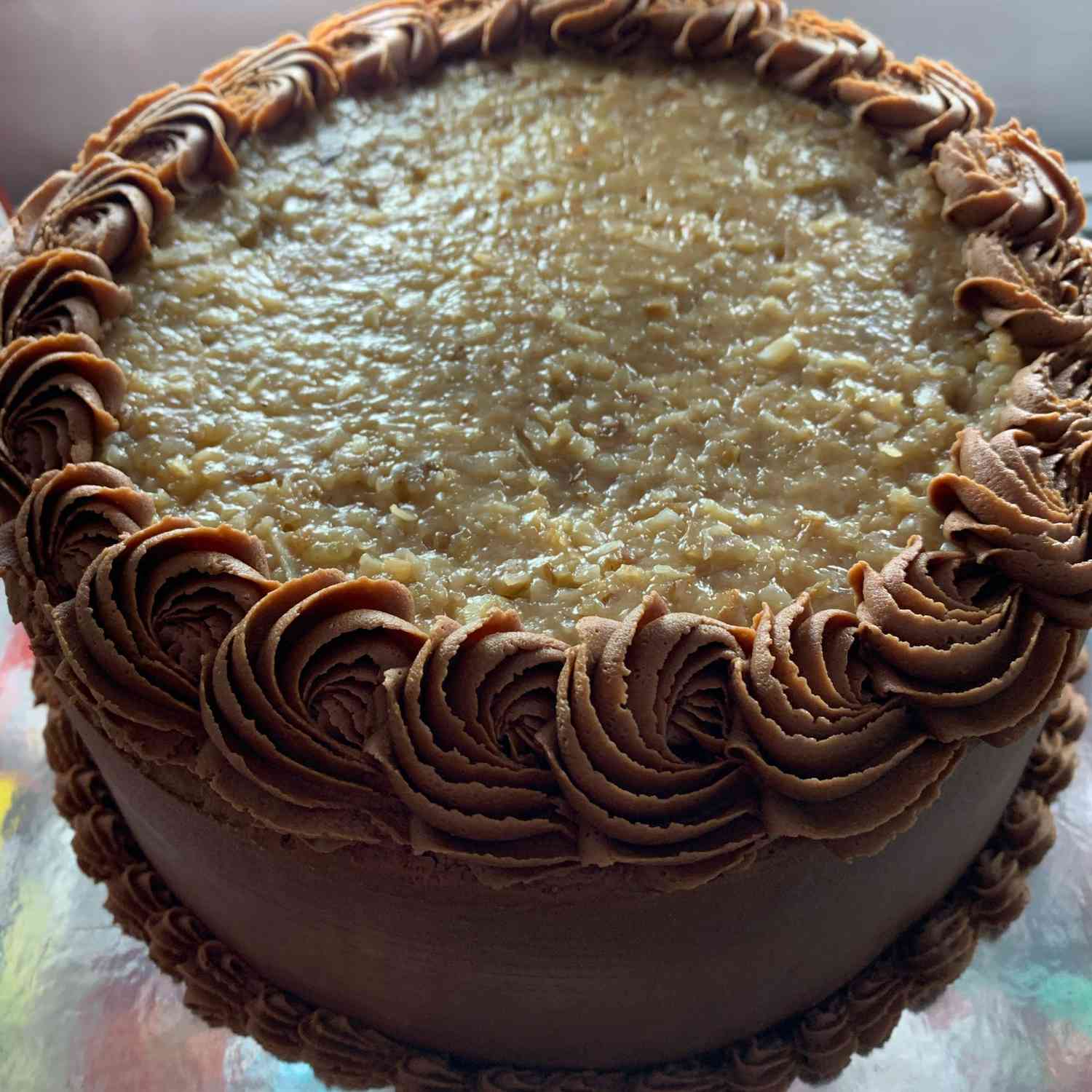 Top-down view of a cake with coconut-pecan frosting on top, with chocolate frosting on the sides and piped chocolate rosettes around the top and bottom edges