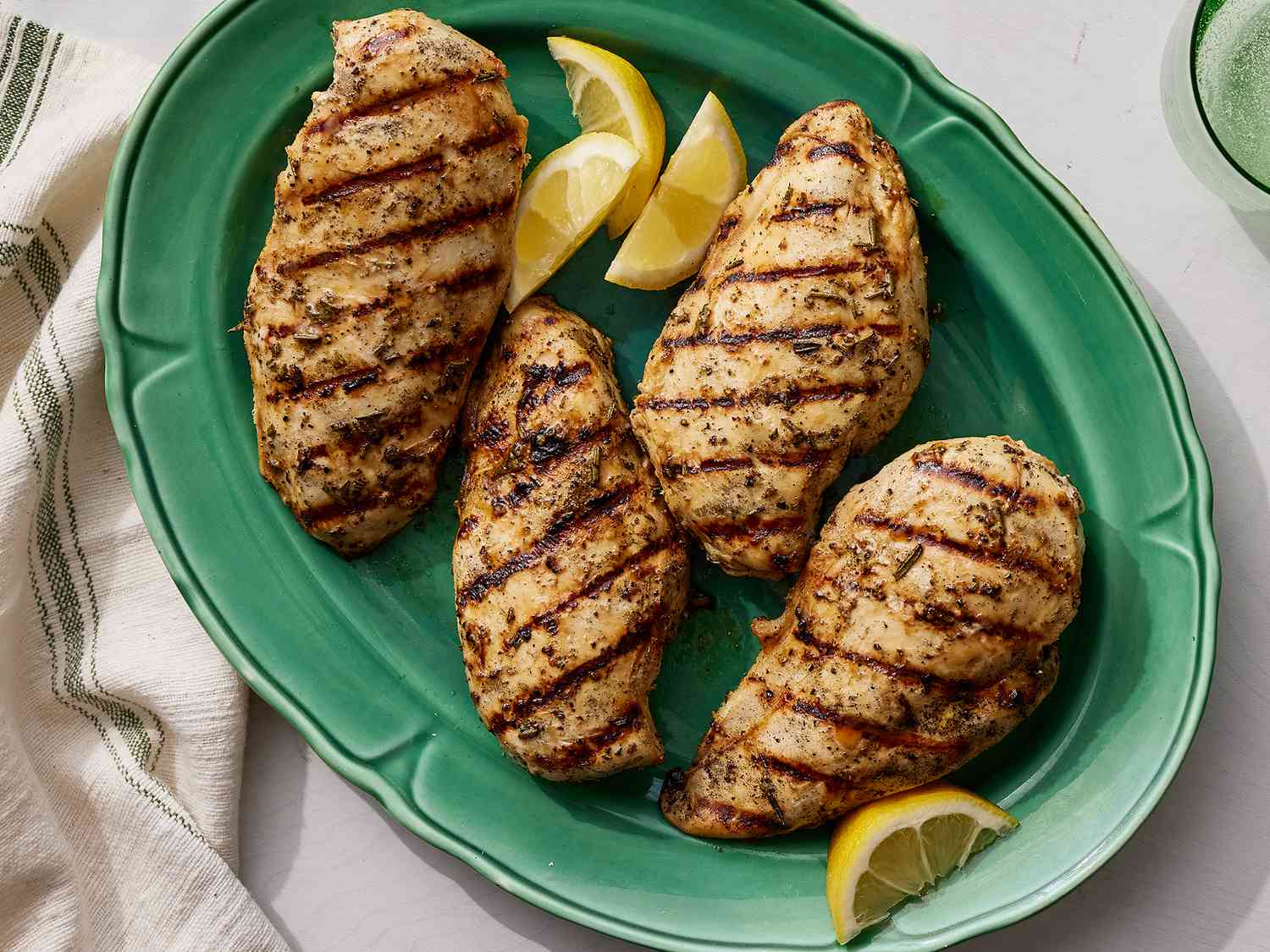 A top down view of 4 grilled lemon pepper chicken breasts on a mint green platter with 4 lemon wedges. 