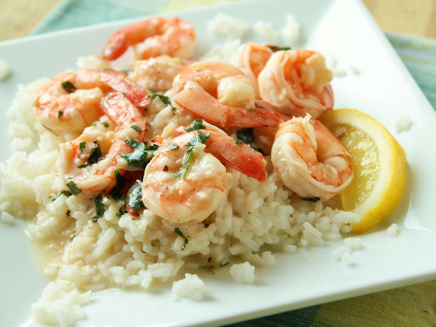 Close up view of Lemony Shrimp over Brown Rice garnished with fresh herbs and a lemon wedge on a white plate