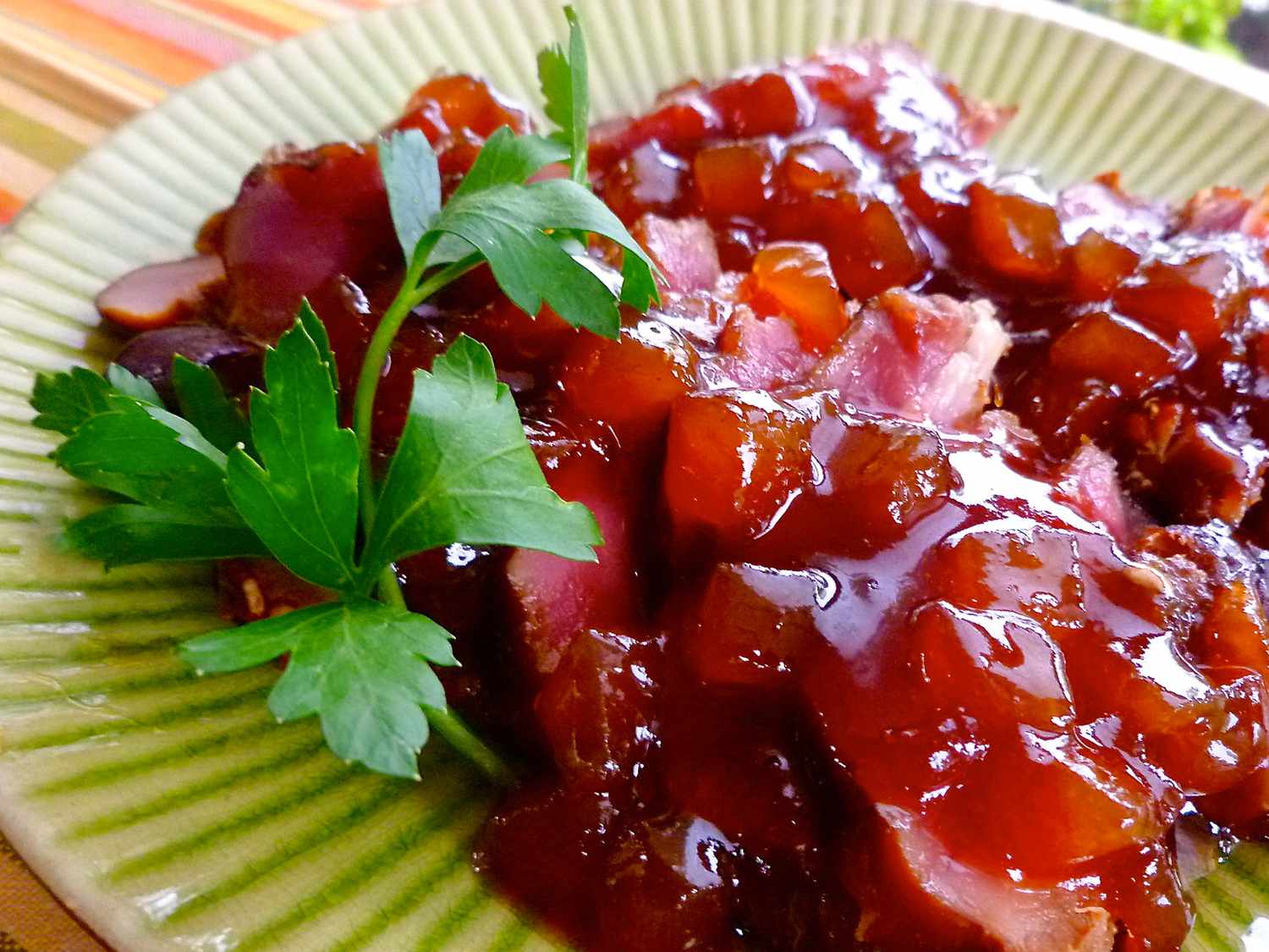 Close up view of sliced Pork Tenderloin with sauce on top, garnished with fresh herbs on a green plate