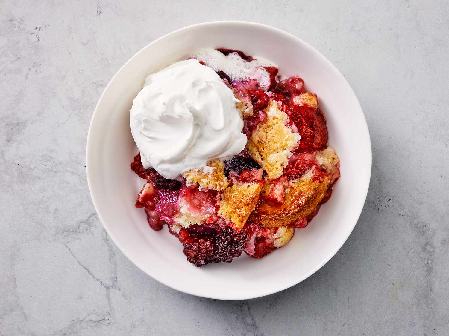 Overhead close up shot of a bowl with berry cobbler topped with whipped cream