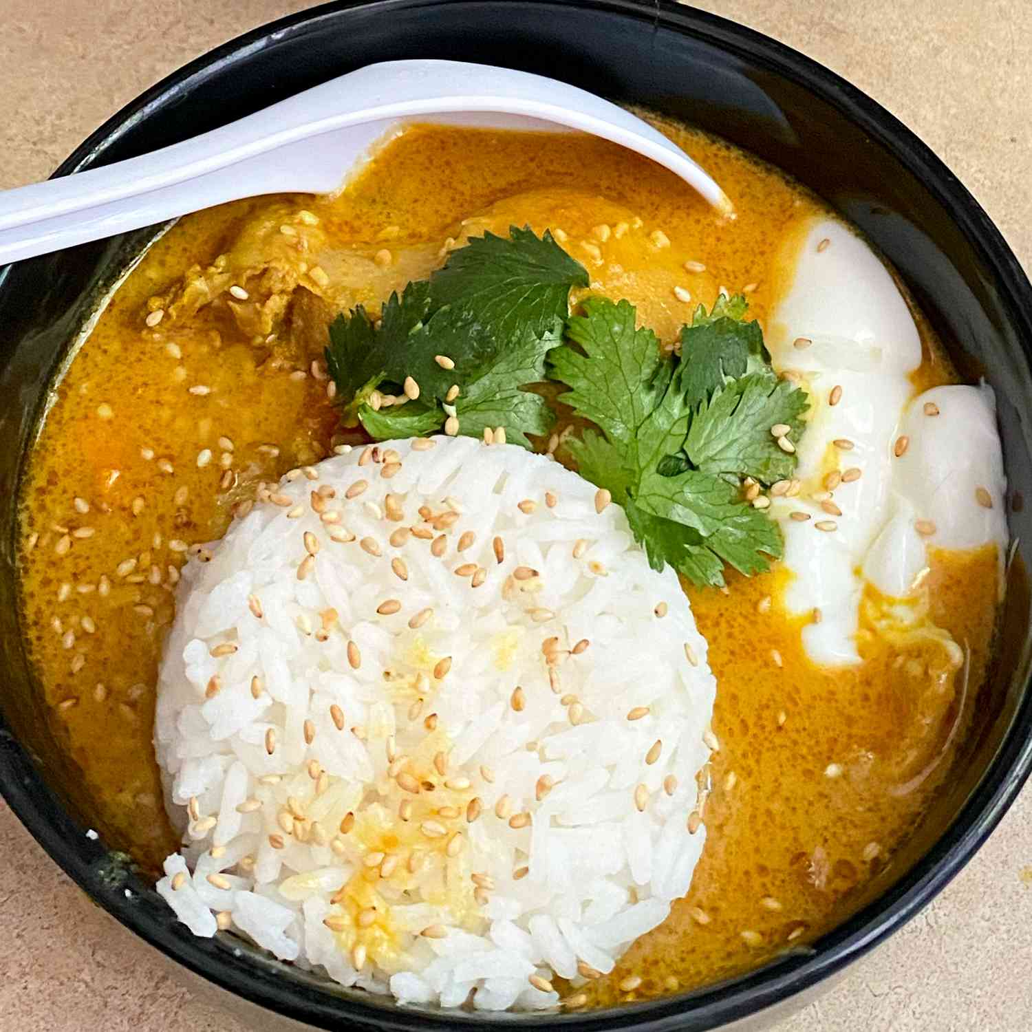 Close up view of Peanut Curry Chicken in a black bowl with white rice and fresh herbs garnished with sesame seeds