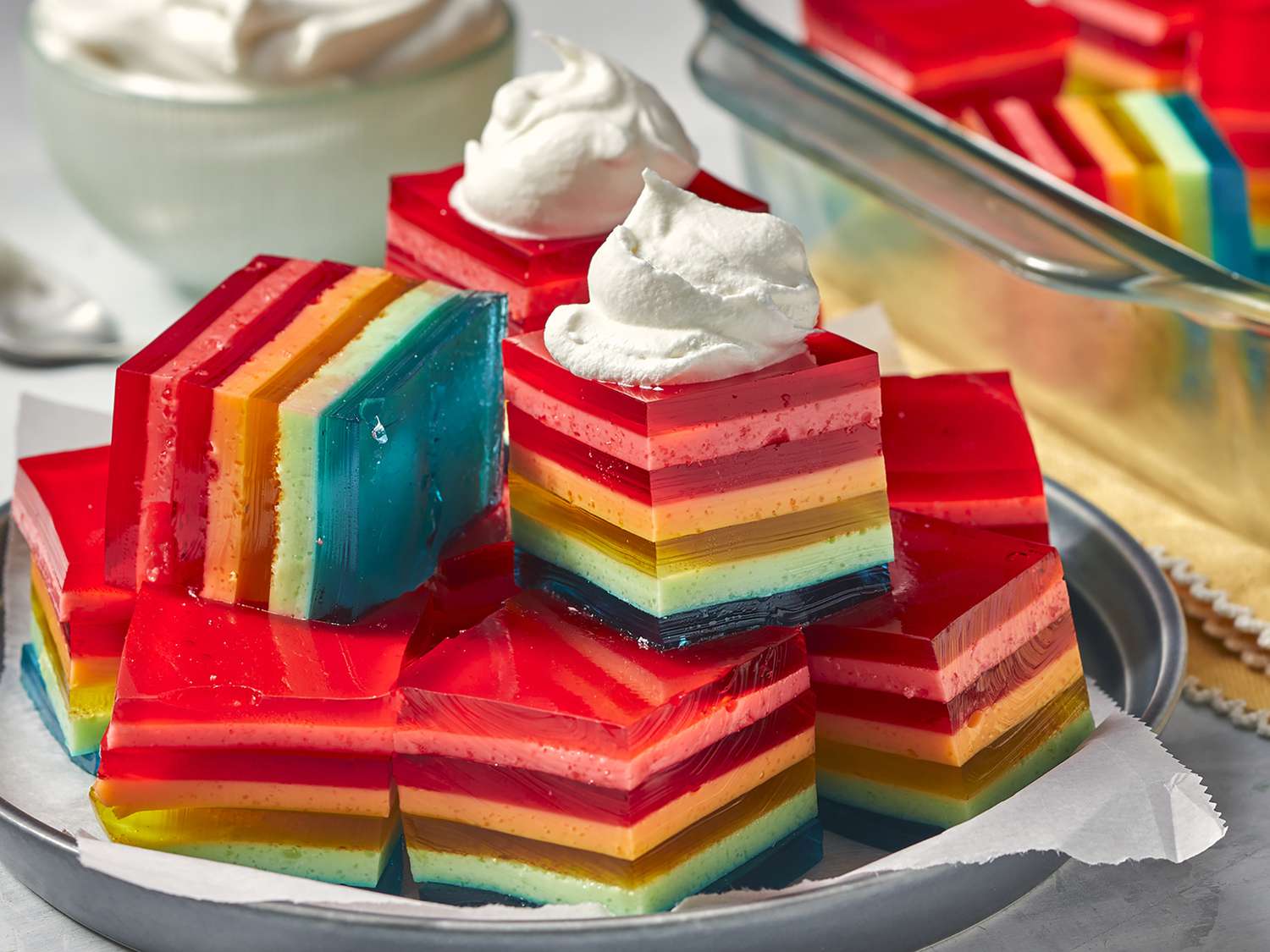 Close up view of a pile of rainbow Seven Layer Gelatin Salad pieces garnished with whipped toping on a platter