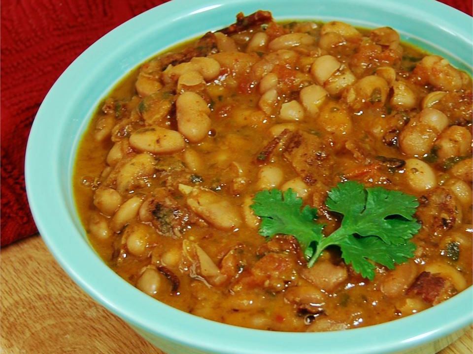 A bowl of pinto beans with tomatoes and bacon, garnished with a cilantro sprig