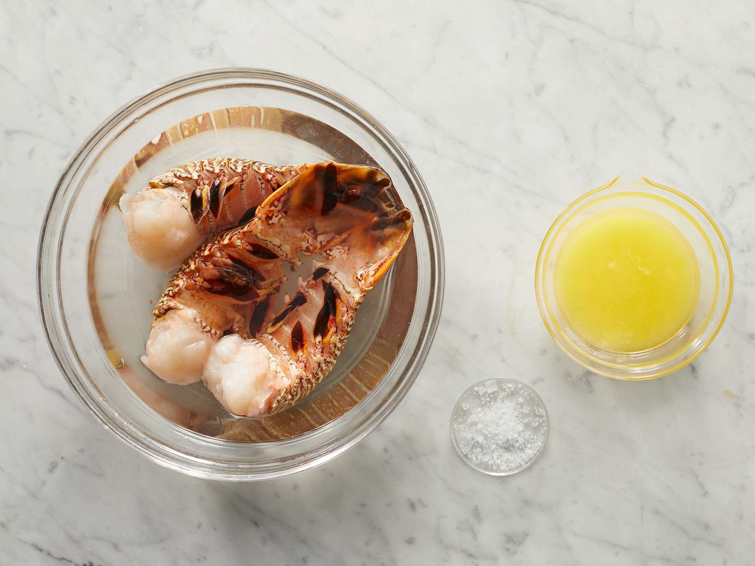 Three lobster tails, salt, and melted butter in glass bowls