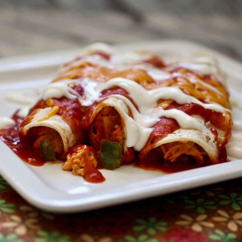 Three chicken enchiladas on a plate topped with red sauce and crema