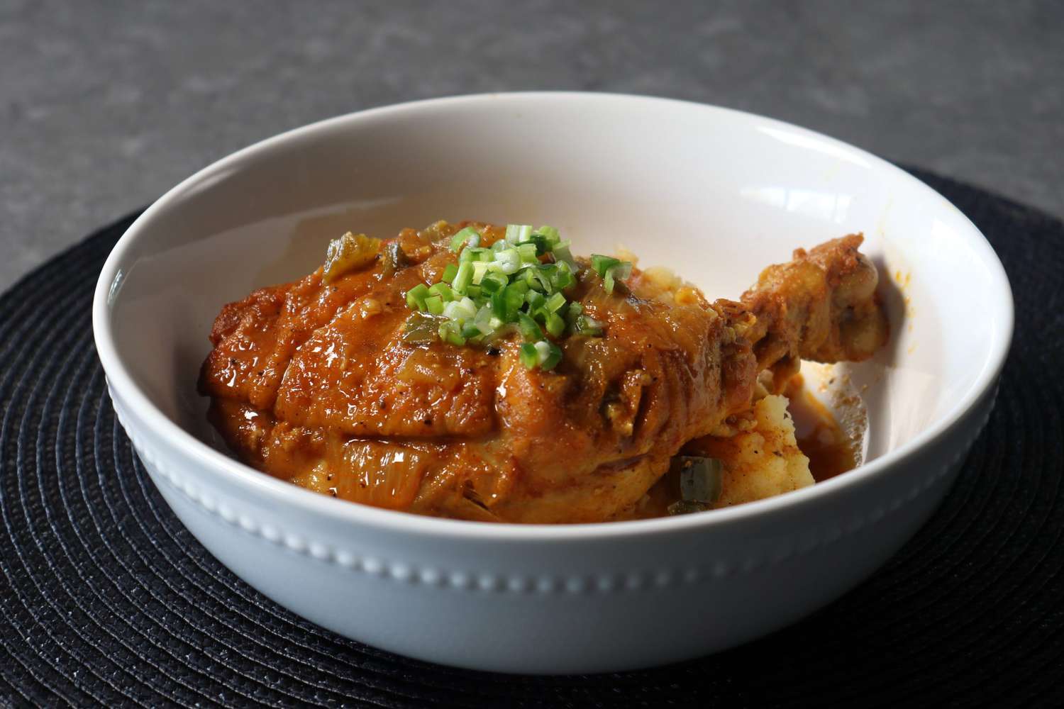 Chicken leg in a golden sauce served over mashed potatoes in a white bowl