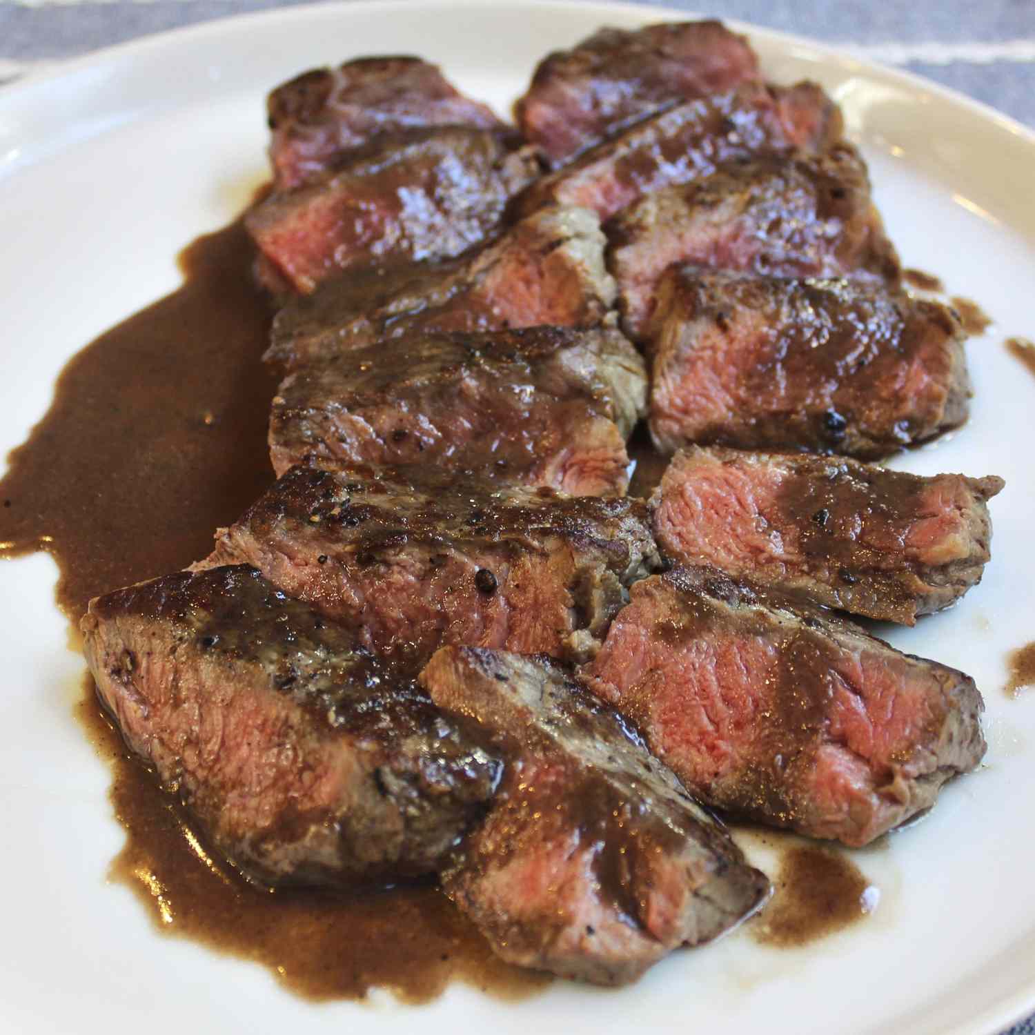 Bite sized pieces of medium rare New York Strips served on a low rimmed white plate and topped with a bordelaise pan sauce