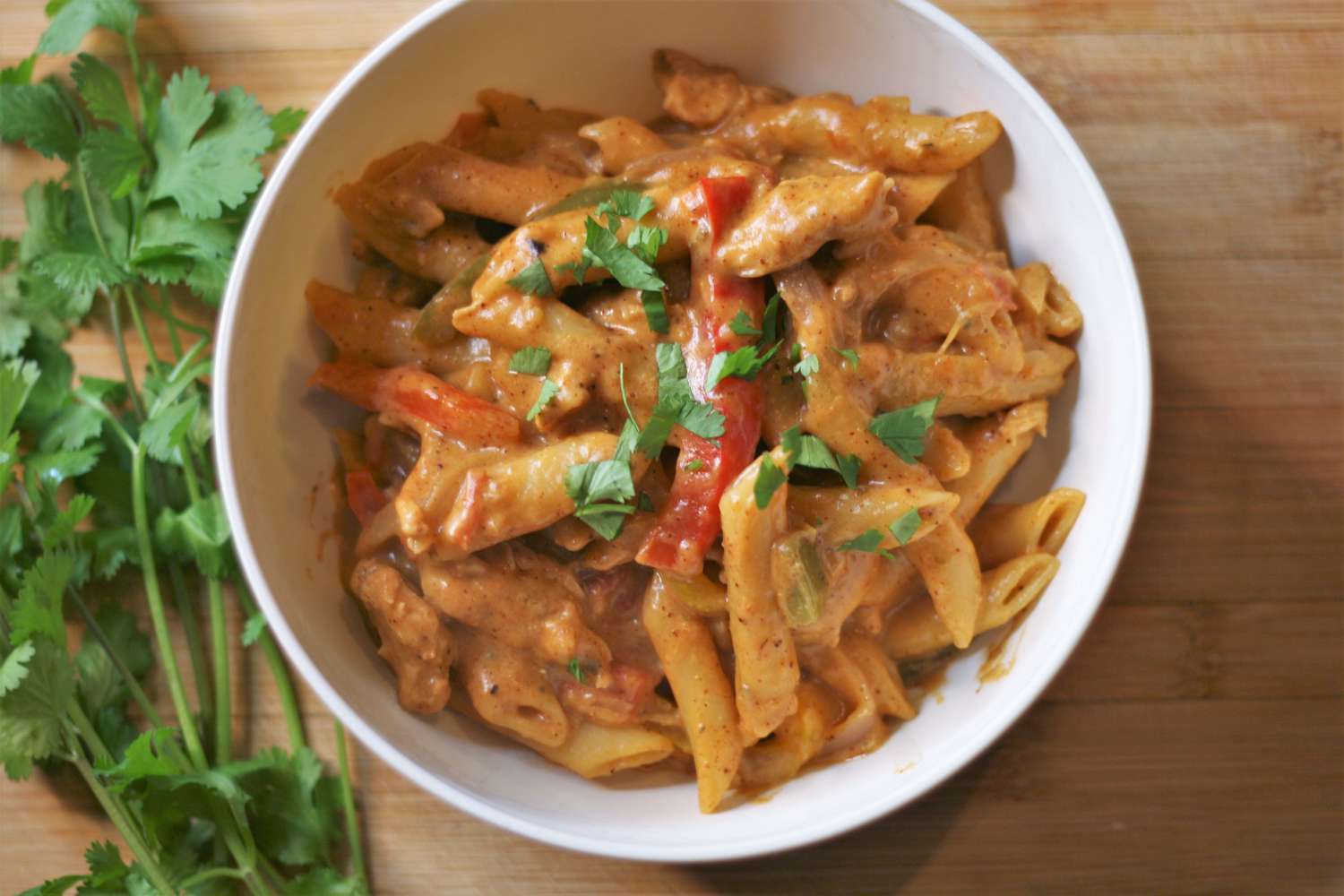 Creamy chicken fajita with penne in bowl with a bunch of cilantro next to it