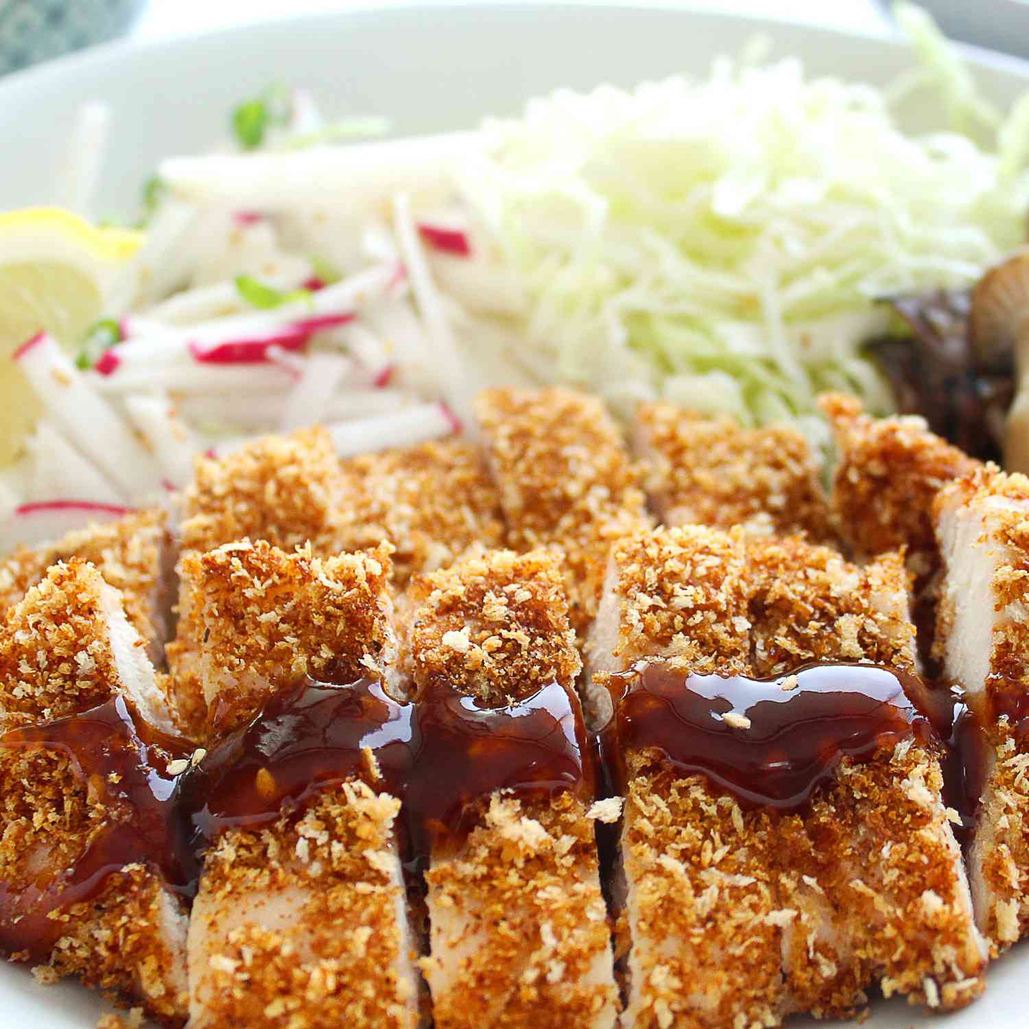 A fried chicken cutlet topped with tonkatsu sauce with salad in the background